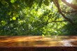 b'An empty wooden table with a blurred background of green leaves.'