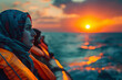 Hopeful Arab refugees in life jackets gaze towards sunset on mediterranean sea