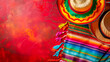 Vibrant backdrop of Cinco de Mayo with traditional Mexican sombreros and colorful serape laid against fiery red textured background, embodying festive joy and cultural pride of Mexico. Copy space