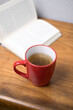 Red Mug of Hot Tea Next to an Open Book on a Wooden Table