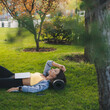 Adult woman sleeping while reading a book and getting bored lying on green grass in the morning park. Lazy and relaxation concept.