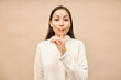 Studio portrait of cute asian woman in turtleneck showing shh gesture pressing index finger against lips, sharing secret recommendations of special offer of discounts, standing against pink background