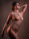 Fototapeta Tęcza - Creative studio portrait of young beautiful woman in beige bodysuit with foreground made of water drops .