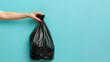Hand holding a black garbage bag on a blue background