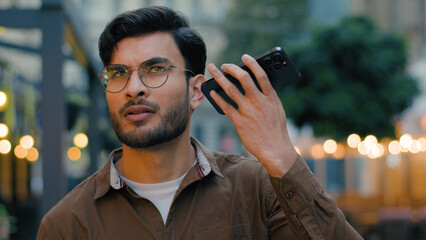 Confused rich businessman Indian Arabian guy ethnic man male using mobile phone device listening voice mail discussing business online meeting call networking bad wifi connection walking city street
