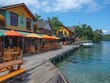 A waterfront area with a wooden pier and a dock. There are several restaurants and cafes along the pier, and a boat is docked in the water. The atmosphere is lively and inviting