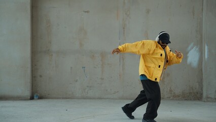 Hipster shows or practicing footstep at street, urban city. Motion shot of young stylish break dancer moving and stretch arm and leg. Outdoor sport 2024. Gray background. Hip hop fashion. Endeavor.