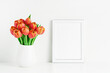 White frame mockup and red tulips in a white vase on a white table by the wall