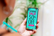 Spring sales offer Ad. Up to 50% off. Woman outdoors holding a mobile phone showing an offer or coupon on the screen.