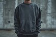 Man in grey sweatshirt with hands in pockets stands by wall