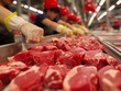 A group of people are working in a meat processing plant. The workers are wearing gloves and red hats. The meat is being processed and cut into smaller pieces. The scene is busy