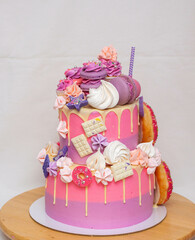 Wall Mural - Pink ombre birthday cake with donuts, meringues and chocolate on neutral background. Cupcake on the top
