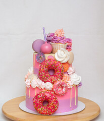 Wall Mural - Pink ombre birthday cake with donuts, meringues and chocolate on neutral background. Cupcake on the top