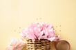 Rattan basket with pink flowers, gift box and coffee cup on pastel yellow background. Happy Mothers Day, International Women's Day, feminine concept.