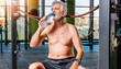 uomo anziano in palestra che beve acqua da una bottiglietta