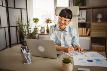 Wall Mural - Mature japanese woman with eyeglasses sit and sign document at the office