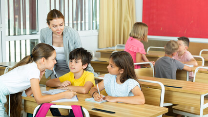 Wall Mural - Group of diligent school kids discussing something in group during lesson in classroom in elementary school