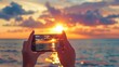 Close-up of a woman's hands with a phone taking photos of a bright sunset and the sea.