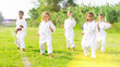 © JackF - Group of kids in white kimono training outdoors on green grass.