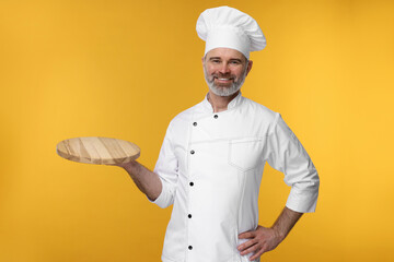 Poster - Happy chef in uniform with wooden board on orange background