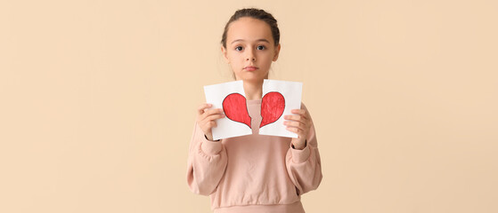 Wall Mural - Sad little girl with torn drawing of heart on beige background. Divorce concept