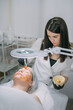 Cosmetologist and dermatologist makes a moisturizing, rejuvenating woman lying patient in a beauty salon.