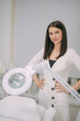 Portrait of a young beautiful woman beautician in a medical white uniform in her office with cosmetology equipment