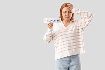 Poster - Mature woman holding paper with word MENOPAUSE on light background