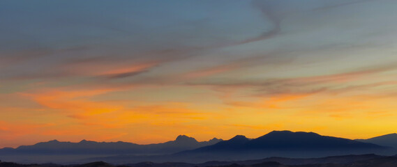 Wall Mural - Luminoso tramonto arancio e ocra sopra le montagne italiane