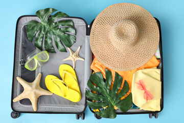 Wall Mural - Open suitcase with beach accessories, palm leaves and starfishes on color background