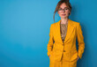 Portrait of a cheerful businesswoman in a yellow suit and glasses posing on a blue background, looking at the camera smiling
