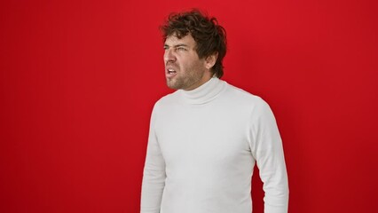 Canvas Print - Enraged young hispanic man, in sweater, furiously screaming. embodies wrath and aggression standing against red isolated background.