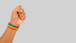A rainbow wristband on the wrist against a gray background.