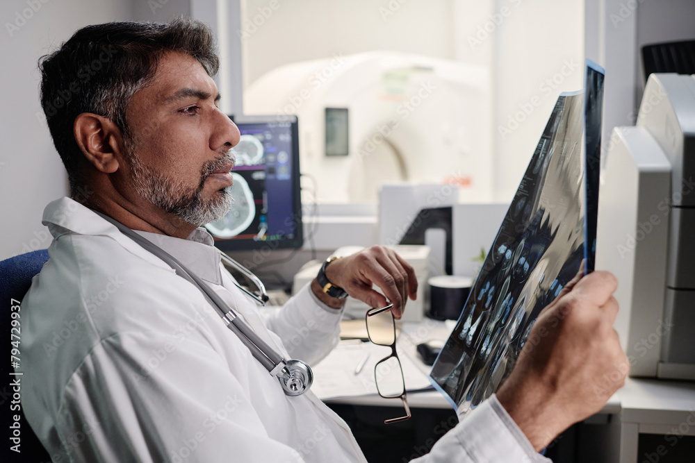Side view of biracial male radiographer sitting at table in office ...