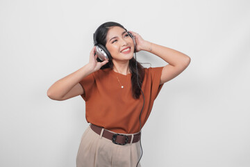 Cheerful young Asian woman in brown shirt enjoying and listening to music using wireless headphone.