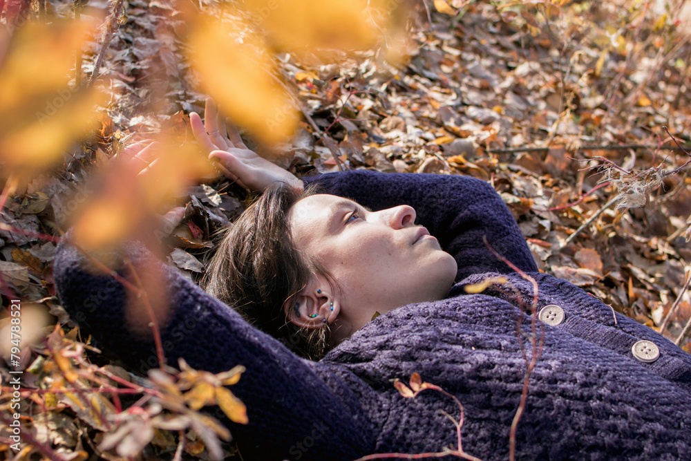 A serene scene of a young woman lying amongst autumn leaves, eyes ...