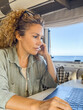 Curly woman looks at her laptop monitor which she uses to communicate with friends and family online. Attractive woman travelling, staying overnight in her camper van at an RV camping area