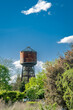 Malerisches Industriedenkmal inmitten üppiger Vegetation: Wasserturm mit Storchennest am Bahnhof von Kremmen, Blick von Südosten