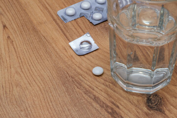 The medicine next to the glass cup. Vitamin pill soluble in water. A pill and empty pack on the table and pills next to it