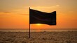   The sun sets over the ocean, a black flag flutters in the foreground, and a sandy beach stretches out A vast body of water lies in the distance