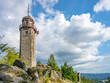 The stone lookout tower of Prosecsky Hreben stands on rocky terrain against a partly cloudy sky, offering a potential view of the surrounding landscape.