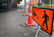 Man Walking Road sign along a closed footpath. Unrecognizable workers in the distance. Roadworks in Auckland.