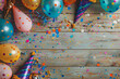 Colourful carnival panoramic banner with a jumble of party balloons, streamers, conical hats and confetti on a wooden table with copy space
