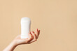 Woman hand holding white body deodorant on beige background, copy space