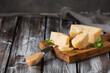 Parmesan cheese pieces on a wooden cutting board, dark wooden background. Side view, selective focus, copy space.