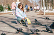 A cute teenage girl feeds pigeons in the park with bread. The girl in the jacket. Spring, the sun.	