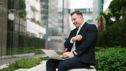 Sticker - Caucasian project manager working on his laptop and celebrate for successful work while sitting at bench in green urban city. Businessman writing report and discussing idea with business team. Urbane.