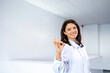 Portrait of smiling beautiful female doctor standing in hospital lobby and holding okay gesture sign.