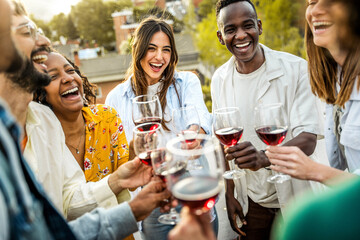 Happy friends toasting red wine glasses outside - Group of young people having bbq dinner party in backyard house