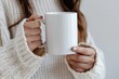 © VICHIZH - Cozy woman in sweater holding white coffee mug mockup in natural light setting at home